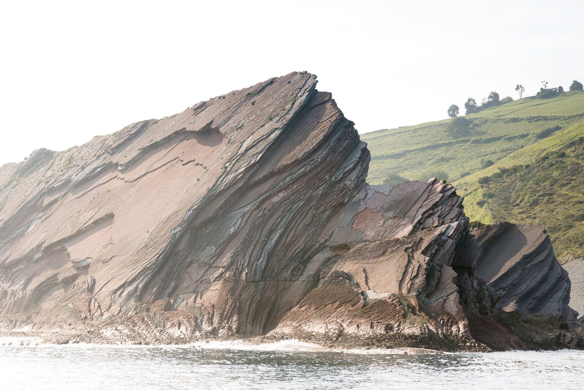 Folded flysch walls falling into the sea below green meadows, Zumaia